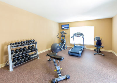 Fitness center at Stallion Pointe with a treadmill, elliptical, stationary bike, racked free weights, and a workout bench